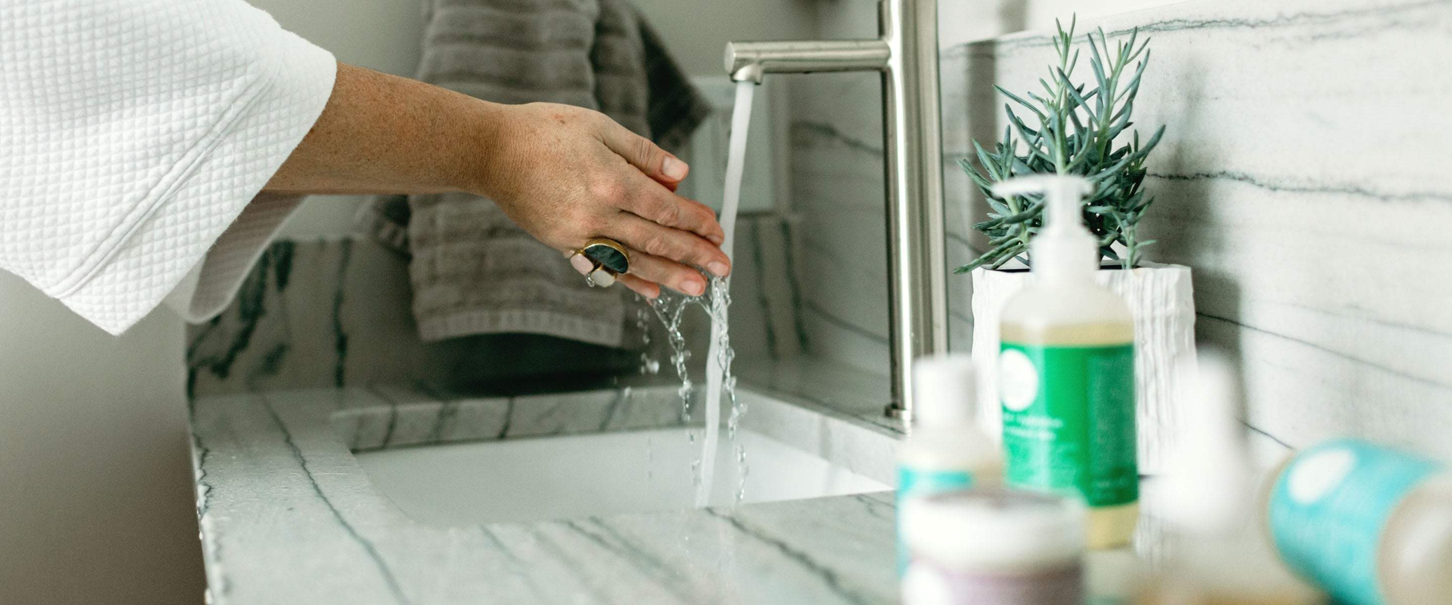 This woman is using our skin care for uneven skin tone at her bathroom sink, that corrects producing too much melanin.