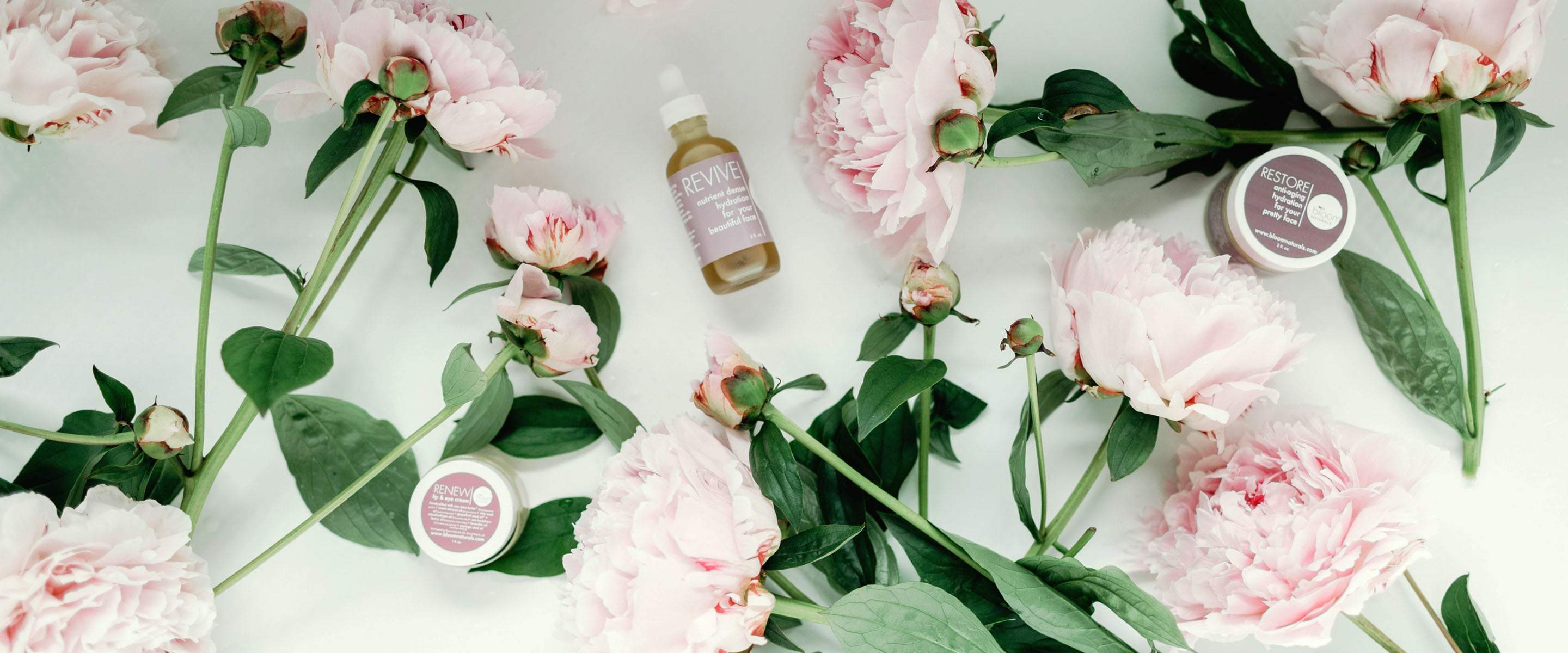 Our products Revive, Renew and Restore sitting on the table with flowers slow the aging and wrinkle process down.